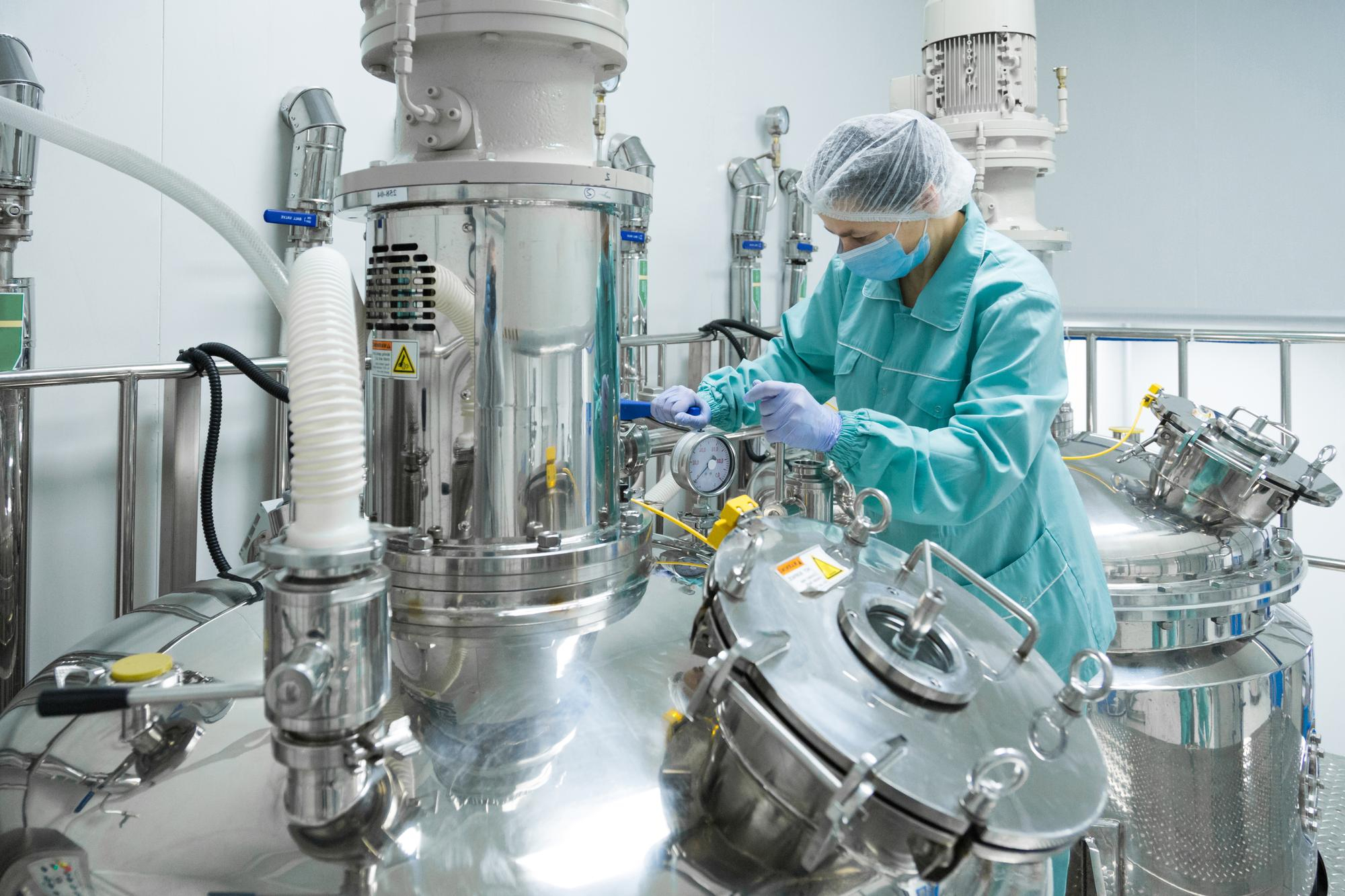 Pharmaceutical manufacturing worker in protective clothing operating bioreactor equipment